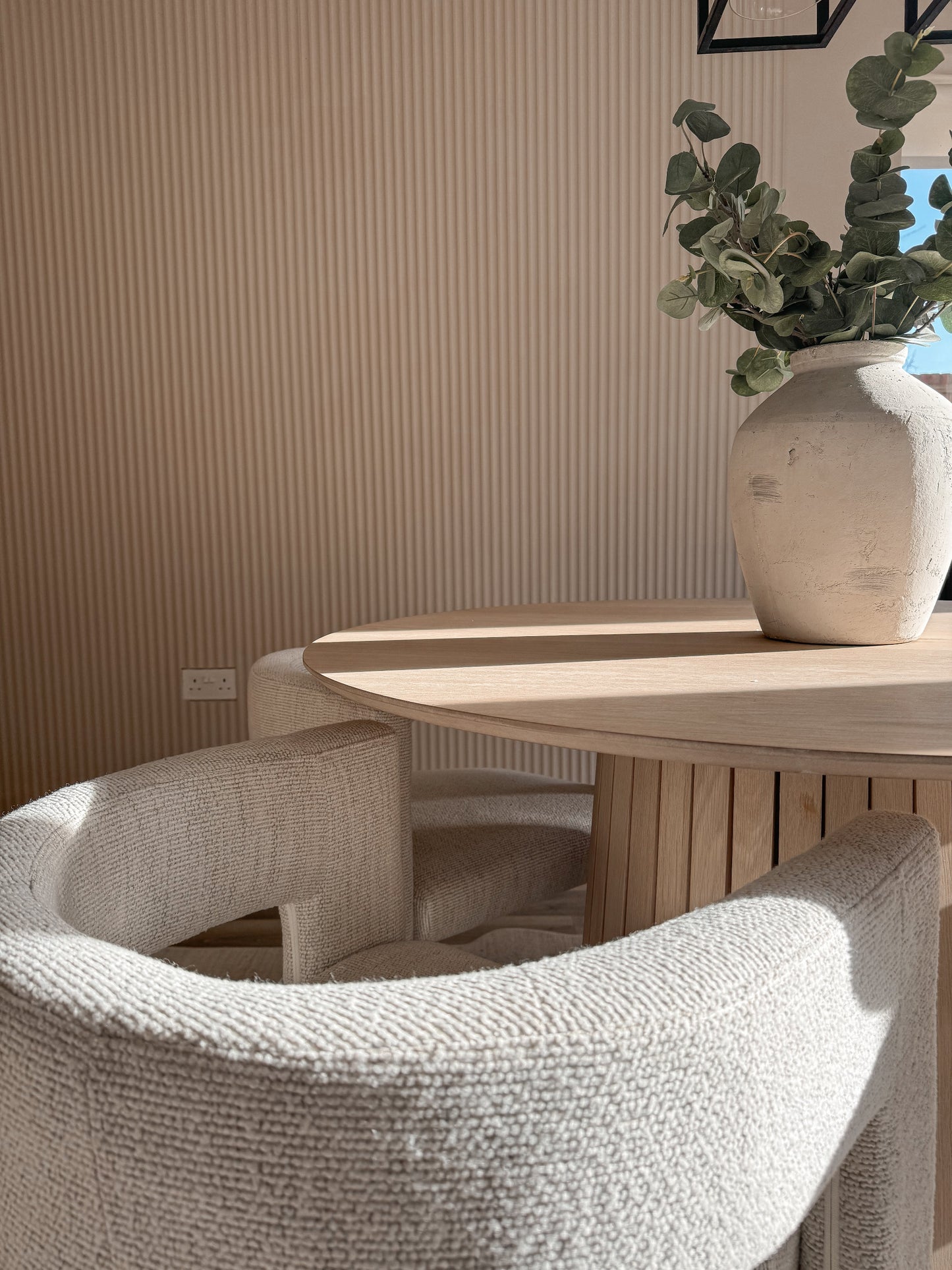 Dining area with a wooden table and chairs, featuring a vase and fluted wall panelling backdrop