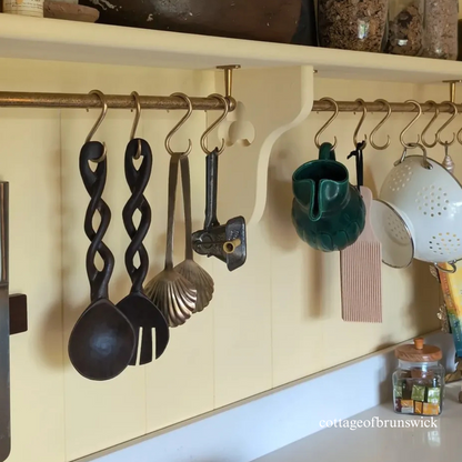 Decorative kitchen utensils and tools hanging on a wall-mounted rack with a tongue and groove panelled yellow wall.