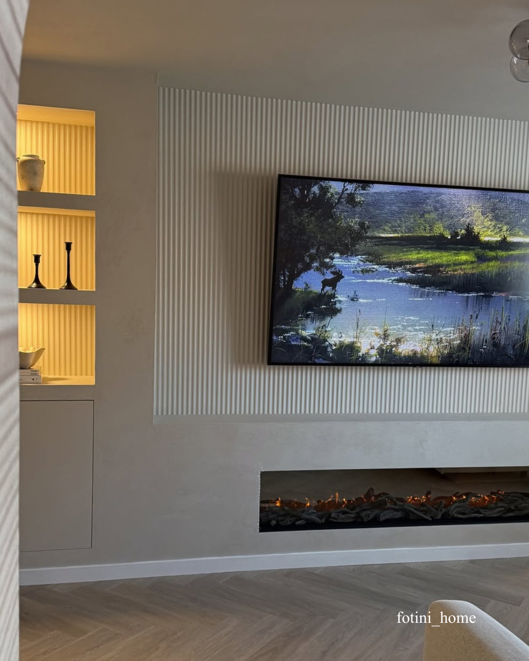 Modern living room with a television displaying a nature scene, a fireplace, fluted wall panelling and a shelf.