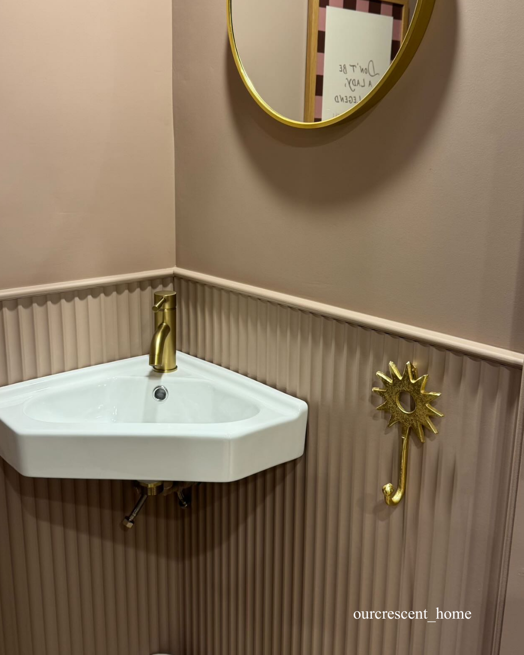 Corner sink with gold faucet and decorative hook on a beige panelled wall