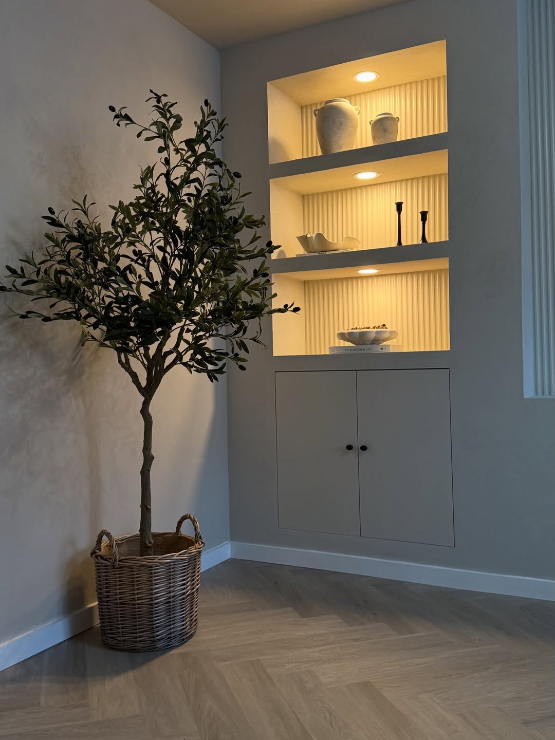 Room interior with a potted plant and a shelf with panelling and decorative items.