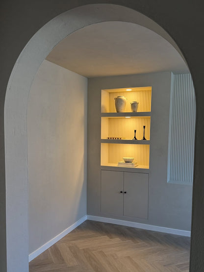 Panelled shelving unit with light interior in a room with an archway