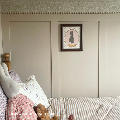 A bedroom featuring Shaker Wall Panelling with a decorative rabbit picture on the wall, beige walls, and a checkered bedsheet.