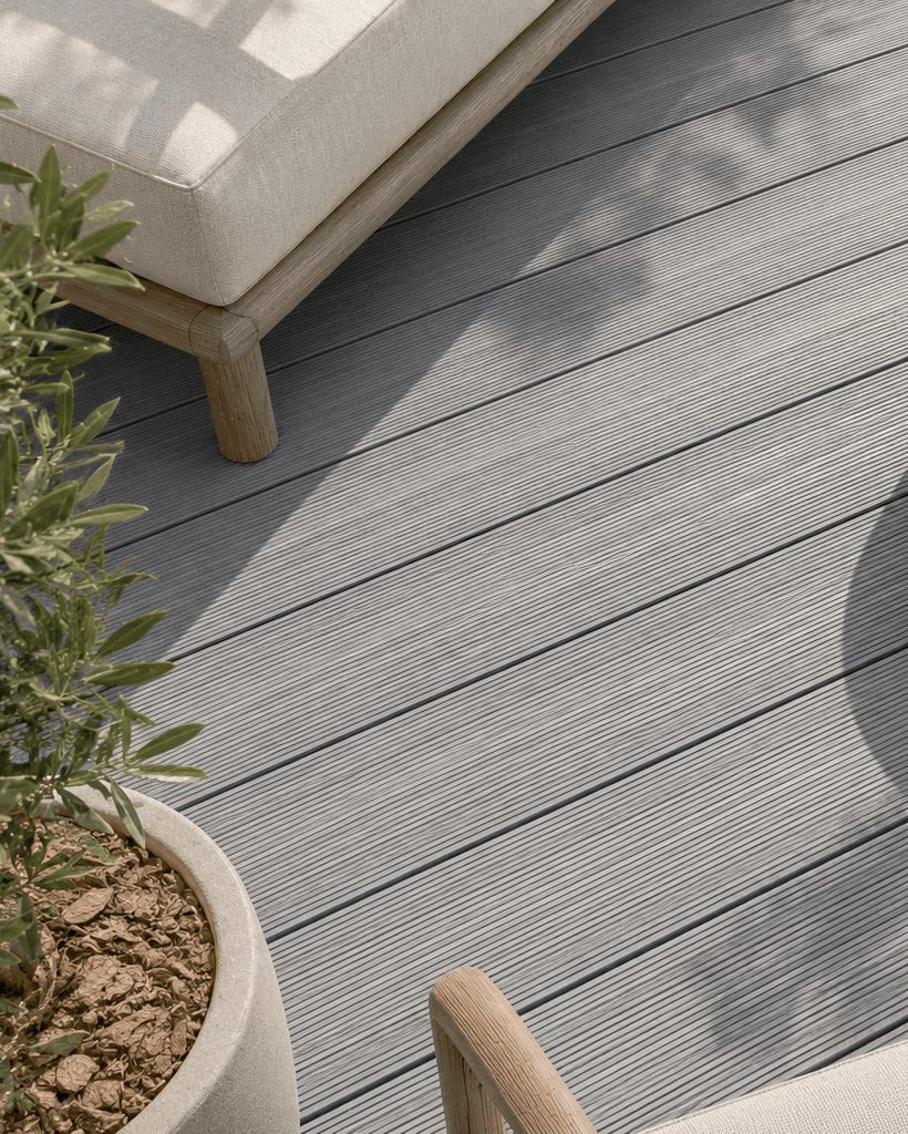 Gray composite decking planks on an outdoor patio with a round concrete coffee table, a white lounge chair, and potted plants.