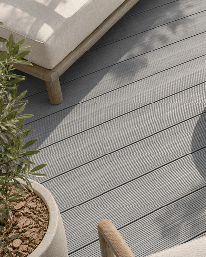 Gray composite decking planks on an outdoor patio with a round concrete coffee table, a white lounge chair, and potted plants.