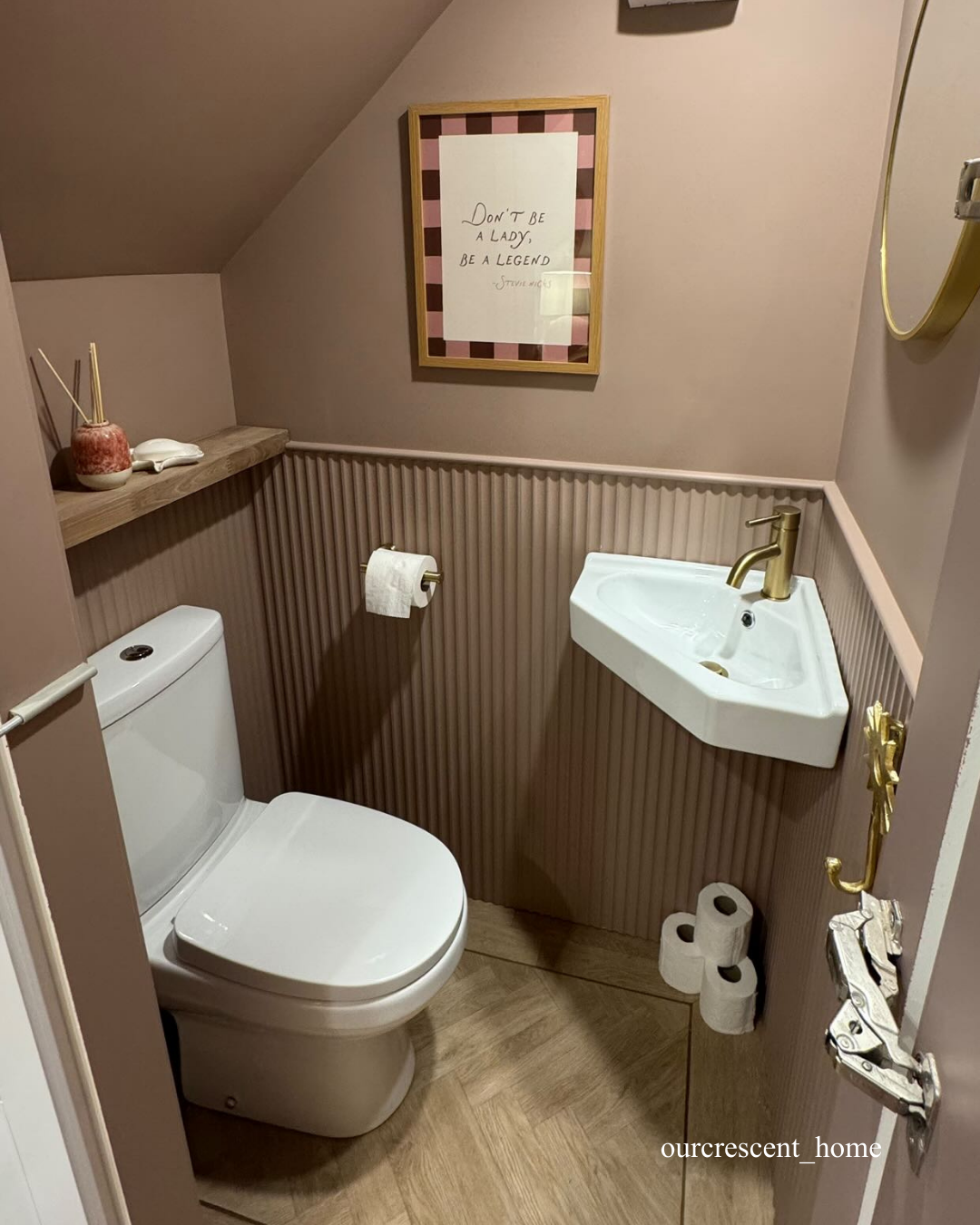 Small bathroom with wall panelling, a toilet, sink, and toiletries on a wooden floor.