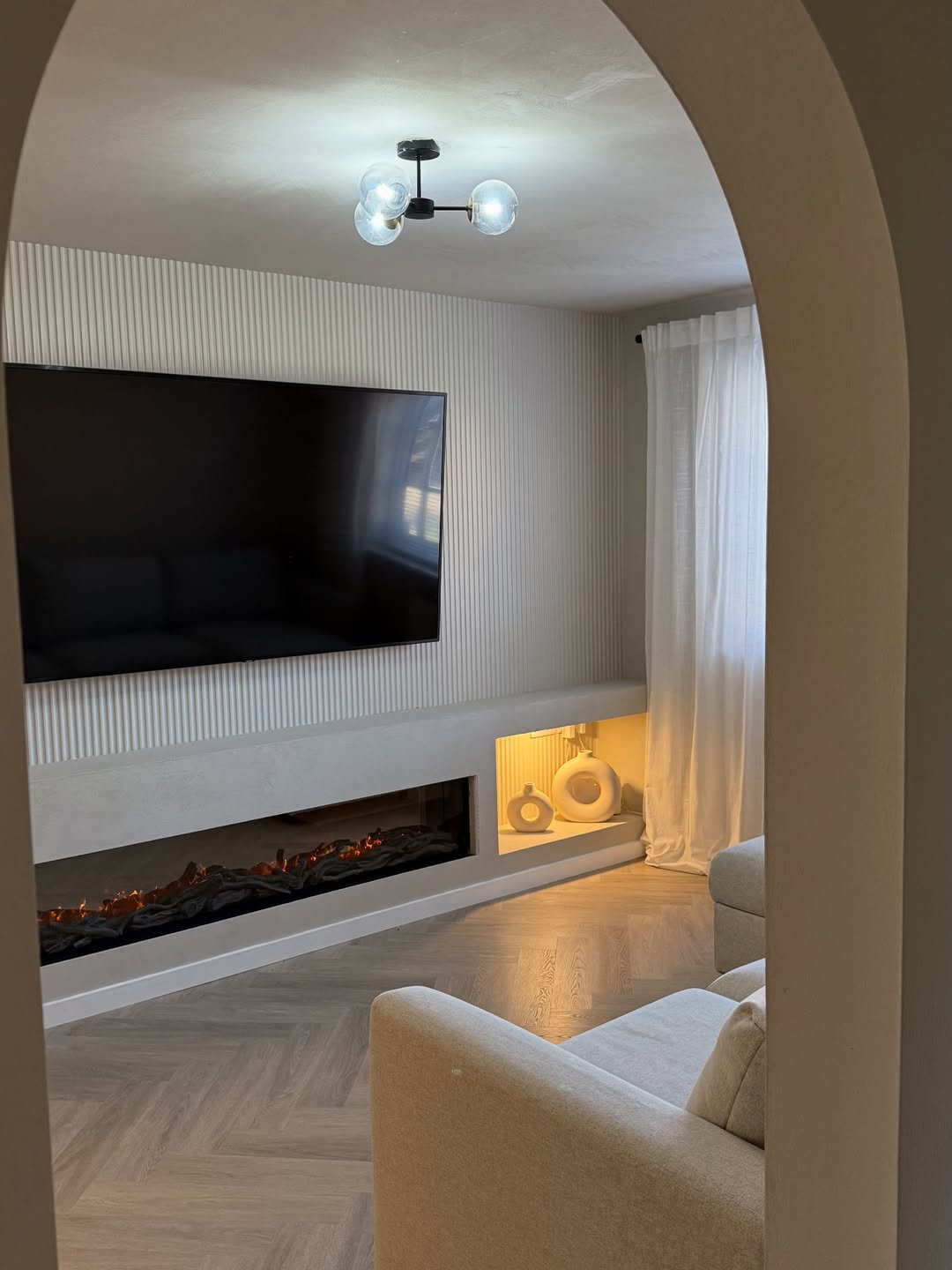 Modern living room with a television mounted on a panelled wall above an electric fireplace.