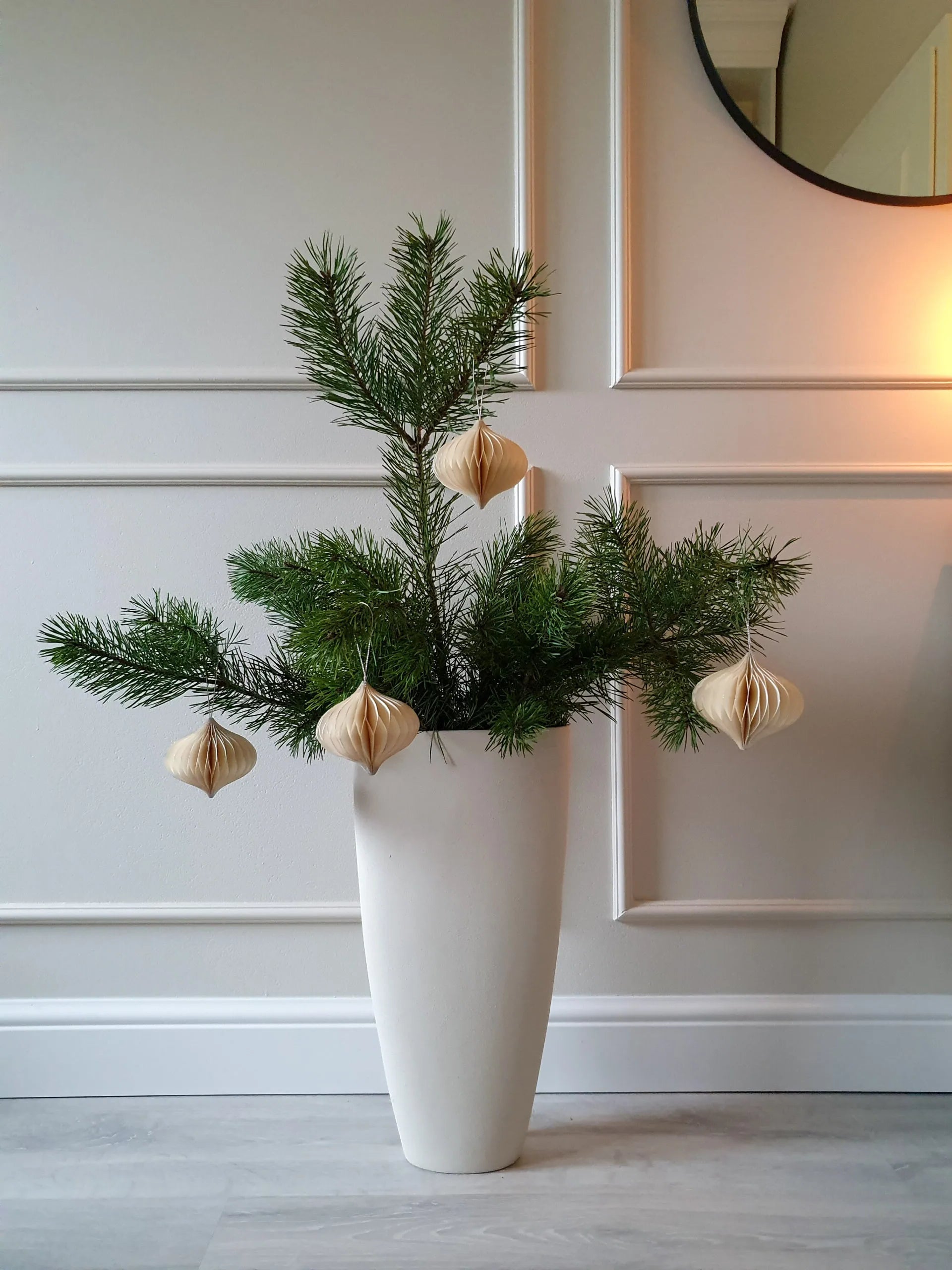White vase with greenery and decorative elements against a neutral panelled wall.