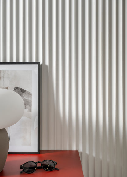 Sunglasses on a red surface with a textured fluted wall and framed picture in the background