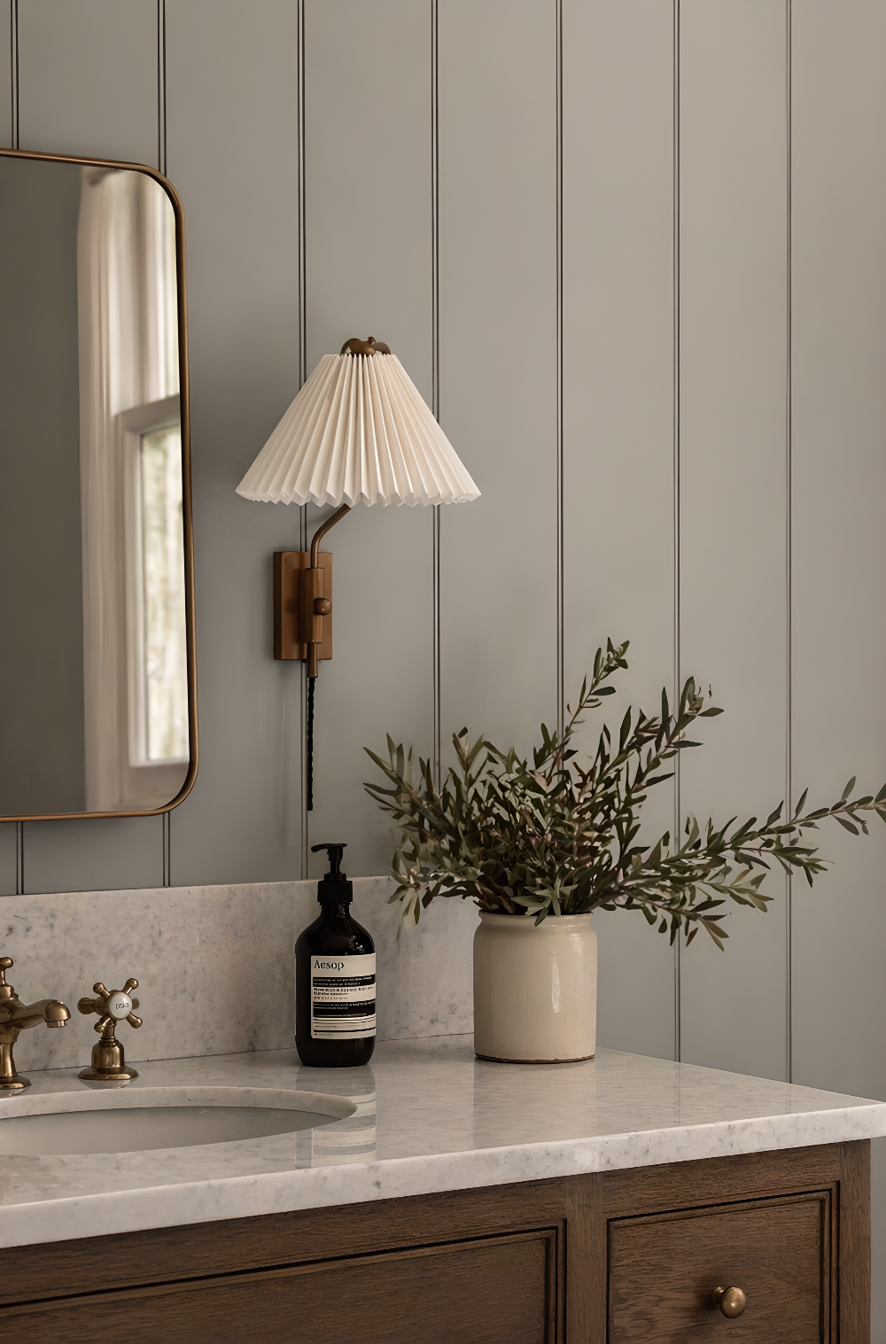 Bathroom with sink, mirror, lamp, and plant against a gray paneled wall.