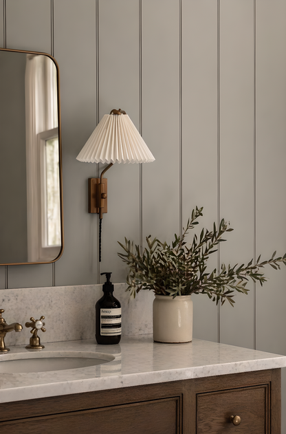 Bathroom with sink, mirror, lamp, and plant against a gray paneled wall.
